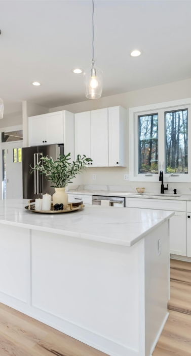Bright modern kitchen featuring white cabinets and island, with minimalist decor.